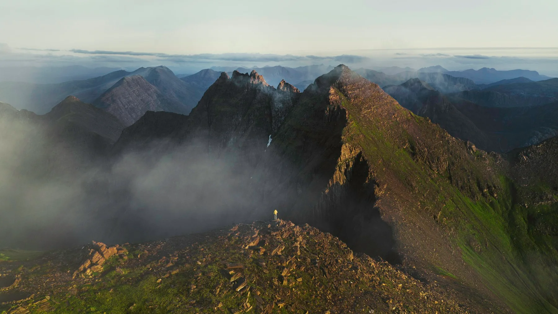 A lone hiker taking in the vast mountains from a rocky ridge in Scotland